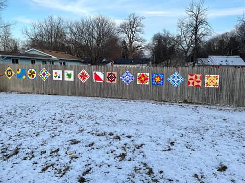 Colorful barn quilt panels mounted on a wooden fence in the snow