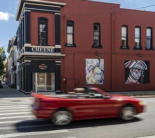 A red convertible passing the mural-covered corner of a downtown Tecumseh building